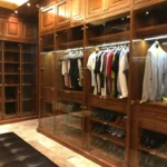 Un armadio in legno su misura con ante in vetro, illuminato da luci integrate, che mostra un'ampia gamma di abiti e scarpe organizzati in modo ordinato.