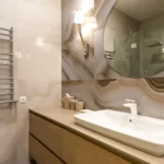 Un moderno mobile bagno su misura realizzato in legno chiaro con lavabo sospeso, specchio a parete e mobiletto sottolavabo con cassetti e ante. Il mobile bagno è completato da faretti a LED e da una finitura elegante e raffinata.